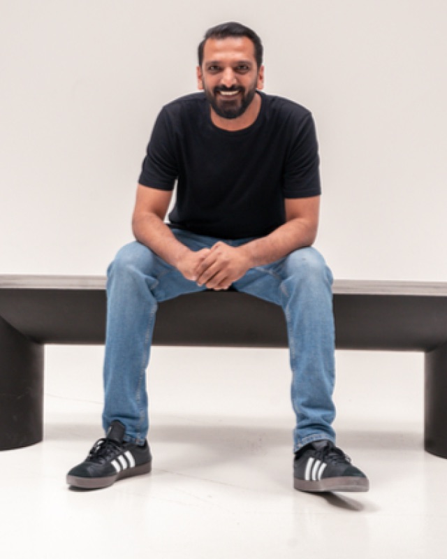 Imran Kapadia, seated on a bench in a white studio